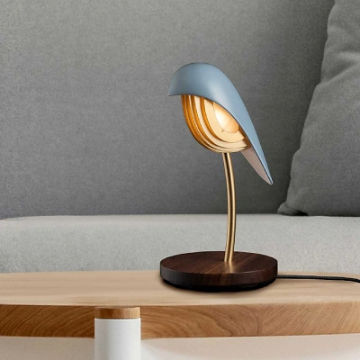 Auf einem kleinen Holztisch vor einem grauen Sofa steht die Bird-Lampe aus blauem Porzellan mit goldenen Akzenten auf einem Walnussholz-Sockel. Das Licht ist eingeschaltet und strahlt eine warme, gem&uuml;tliche Stimmung aus.