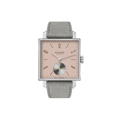 Nomos Tetra mit markant eckigem Design und rosa Zifferblatt. Strichindizes und arabische Zahlen sorgen f&uuml;r klare Ablesbarkeit. Die kleine Sekunde bei 6 Uhr tr&auml;gt einen gelben Zeiger. samtgrauem Velourslederband rundet den Look ab.