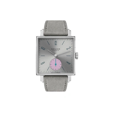 Nomos Tetra mit markant eckigem Design und grauen Zifferblatt.Blauen Strichindizes und arabische Zahlen sorgen f&uuml;r klare Ablesbarkeit. Die pinke kleine Sekunde bei 6 Uhr tr&auml;gt einen blauen Zeiger. Mit einem grauen eganen Veloursband rundet den Look ab.